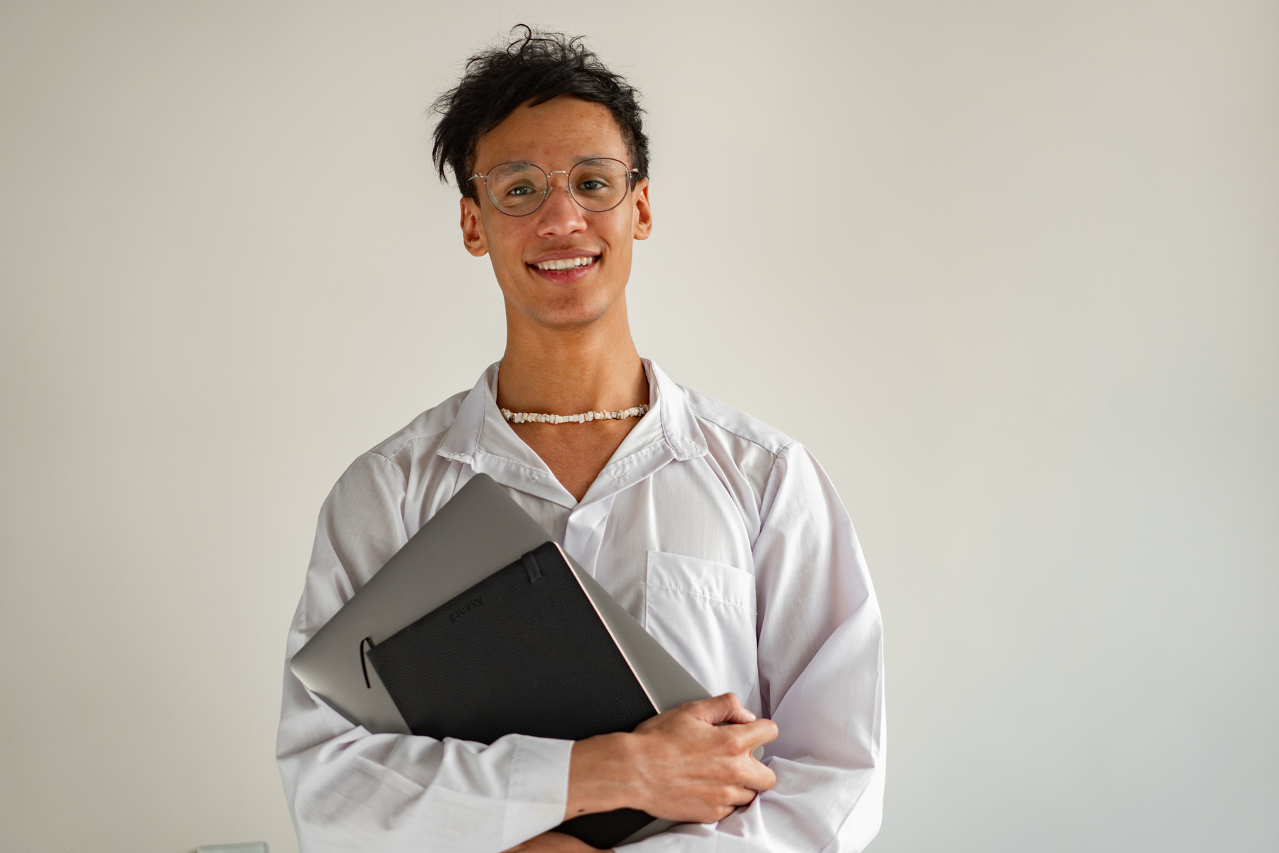 A Man wearing Eyeglasses holding Laptop and Notebook